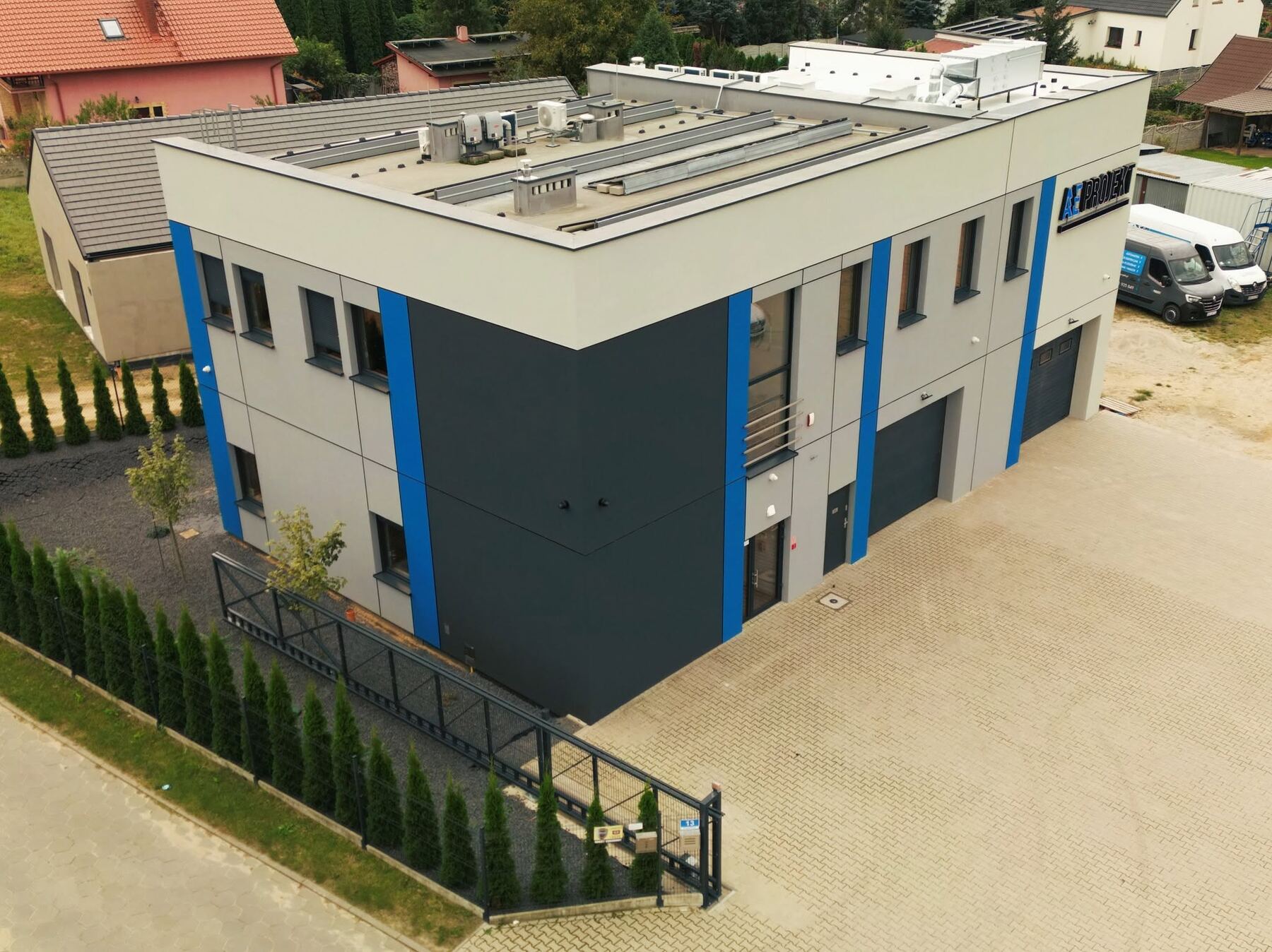 Siedziba AE Projekt w Osiecznej z lotu ptaka: budynek z niebieskimi pionami i oznakowaniem AE, plac i bramy garażowe